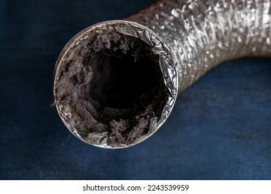 A dirty laundry flexible aluminum dryer vent duct ductwork filled with lint, dust and dirt against a blue background.