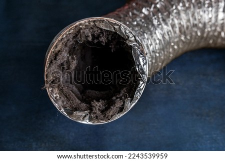A dirty laundry flexible aluminum dryer vent duct ductwork filled with lint, dust and dirt against a blue background.