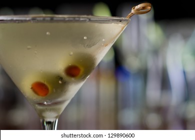 dirty martini chilled and served on a busy bar top with a shallow depth of field and color lights and glasses in the background