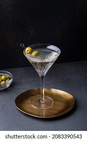 Dirty martini cocktail in martini glass with olives garnish on dark table