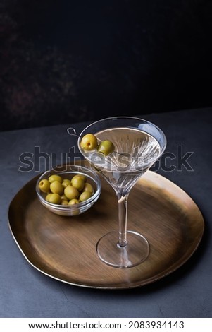 Dirty martini cocktail in martini glass with olives garnish on dark table