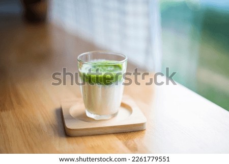 dirty matcha in the glass on the saucer and wood table with windown background.