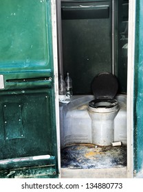 Dirty and neglected chemical toilet booth positioned in a construction site.