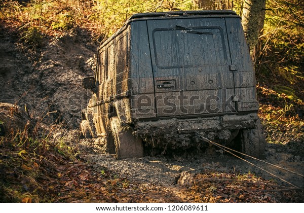 Dirty offroad car stuck in dirt\
on sunny autumn day. SUV with car winch on countryside road.\
Crossover on nature background, reverse, back view. 4x4 racing\
concept.