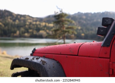 Dirty offroader is parked near lake and forested mountains. Close-up of muddy red SUV and panoramic view of river and hills. Concept of extreme travel and outdoor adventures. - Powered by Shutterstock