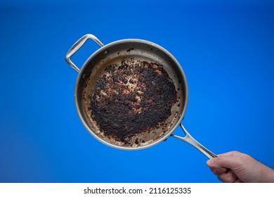 Dirty oily burnt metal frying pan held in hand by male hand.
