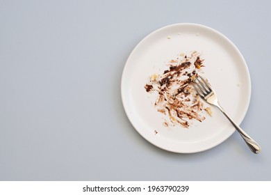 Dirty plate with cake leftovers and fork on gray background, top view