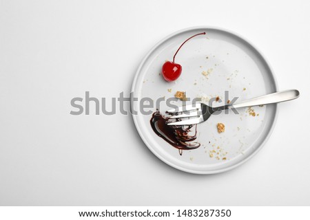 Dirty plate with food leftovers, fork and canned cherry on white background, top view
