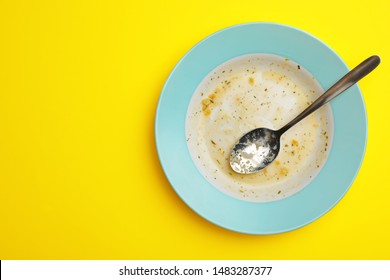 Dirty Plate With Food Leftovers And Spoon On Yellow Background, Top View. Space For Text