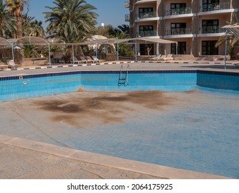 A Dirty Pool With No Water On The Background Of Palm Trees And An Empty Hotel.