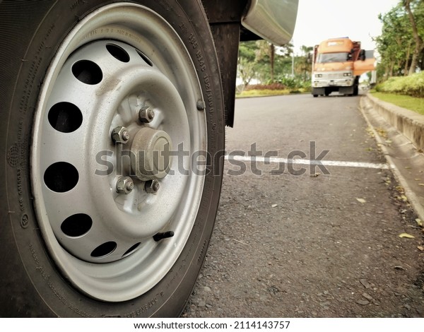 Dirty rear wheel of a truck (tire\
brand removed) with a background of a defocused parking\
truck