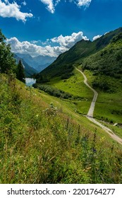 dirty road up over the green and flowered pastures from the great valley of Walser, past alpine farmhouses, alpine huts, trees and forests, up the steep mountain slopes to the mountain lake. sunny day