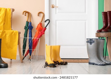 Dirty rubber boots with umbrellas near color wall in hallway - Powered by Shutterstock