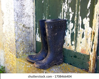 Dirty Rubber Work Boots On The Concrete Floor Against The Background Of An Old Wooden Door
 