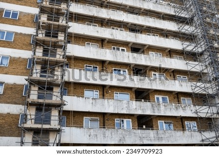 Dirty and rundown residential apartment block in poor area of relative deprivation covered in scaffolding and undergoing renovation
