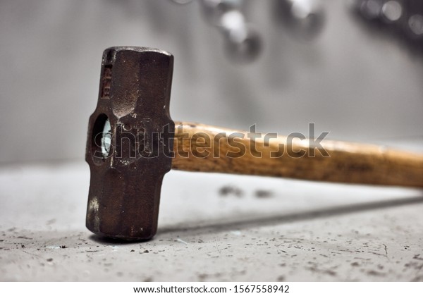 Dirty and rusty metal sledgehammer with\
wooden handle standing on the work\
table.