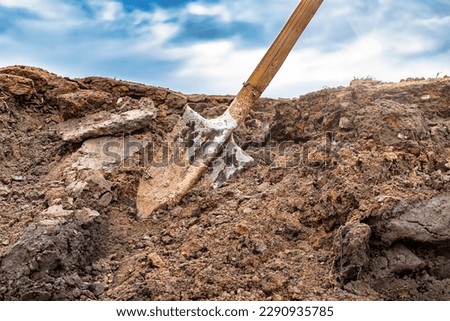 Dirty shovel in fresh soil at a construction site in a pit. Deep hole in the ground. Earthworks, manual refinement of the soil. Dig deep ditches and holes