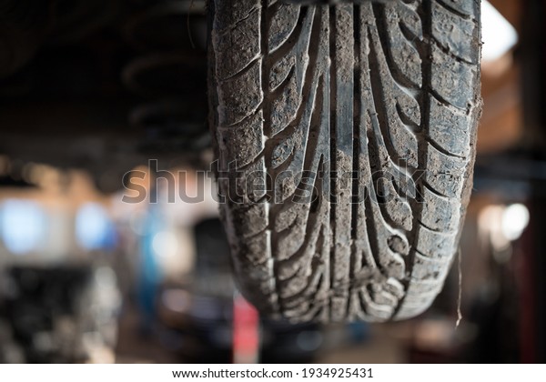 Dirty tire on a lifted\
car in the garage, car tire covered with dust. Close-up. Auto\
service industry.