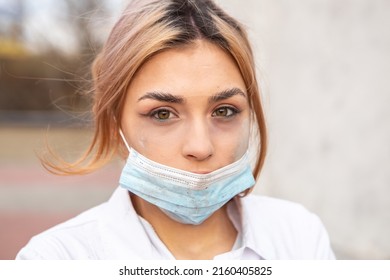 Dirty tired exhausted nurse with ash on face sitting outside hospital infirmary after hard working day or surgery. Doctor woman dressed white medical gown, face mask have a rest due to stress