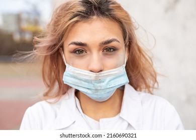 Dirty tired exhausted nurse with ash on face sitting outside hospital infirmary after hard working day or surgery. Doctor woman dressed white medical gown, face mask have a rest due to stress
