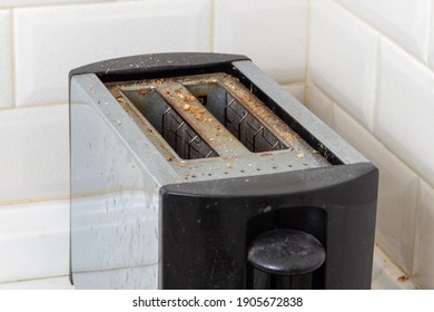 Dirty Toaster With Burnt Crumbs On The Kitchen Table Against The Background Of Light Tiles