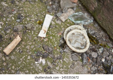 A dirty used rubber condom, surrounded by broken glass and cigarette butts, discarded in a dirty city alleyway. Safe sex prostitution sexual health. sexual disease prevention. 