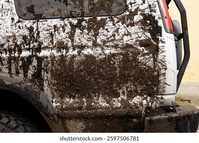 Dirty vehicle with mud splatters on the body, wheels tires, rear bumber. Closeup of a muddy offroad suv car covered in dirt. Importance of car wash, maintenance, and safe driving concept
