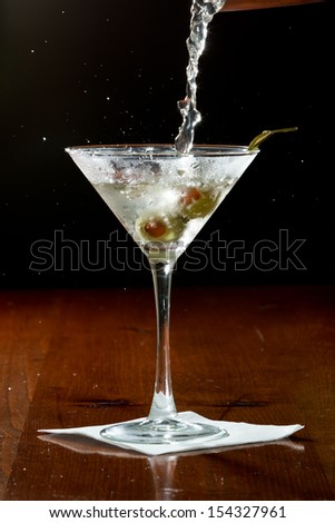 dirty vodka martini splashing into a cocktail glass with green olives