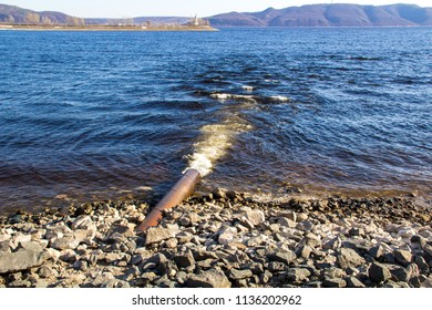 Dirty water flows out of a large metal rusty pipe under pressure into the river.