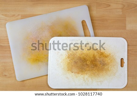 Dirty white plastic cutting board with dark stains, scratch, on wooden background
