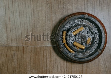 Dirty wooden ashtray with cigarette butts on wooden table background from above. Copy space.