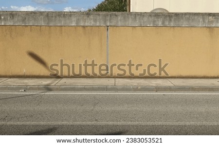 Dirty yellow plaster surrounding wall with a facade and blue cloudy sky on behind. Concrete sidewalk and street in front. Background for copy space.