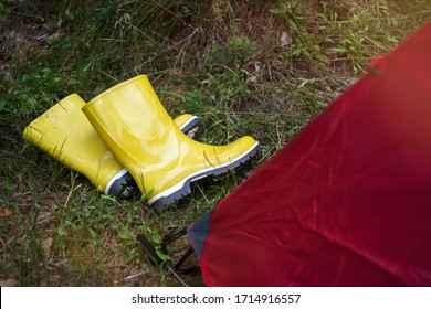 Dirty yellow rubber boots with a white border lie on the wet grass near the tent in a tourist camp.Summer time