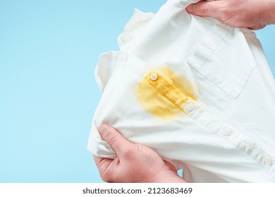 Dirty yellow stain on clothes. men's hands showing a white shirt. space for text. isolated. on blue background. top view. High quality photo