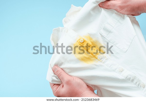 Dirty yellow stain on clothes. men\'s hands showing\
a white shirt. space for text. isolated. on blue background. top\
view. High quality photo
