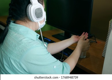 Disability Blind Person With Headphone Wearing Face Mask Applying Alcohol Gel Hand Sanitizer On Hands Before Using Computer With Braille Display Amid Coronavirus (COVID-19) Pandemic.