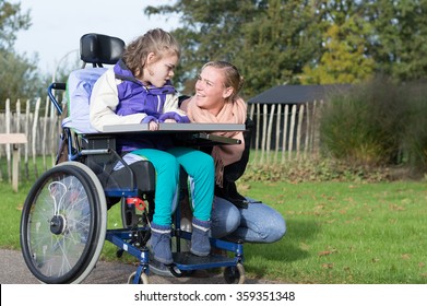 Disability A Disabled Child In A Wheelchair Relaxing Outside Together With A Carer / Disability A Disabled Child Relaxing Outside With A Carer