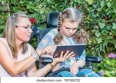 Disability a disabled child in a wheelchair sitting outside looking at a tablet computer together with a voluntary care worker - Shutterstock ID 787300732