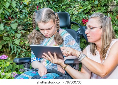 Disability A Disabled Child In A Wheelchair Sitting Outside Looking At A Tablet Computer Together With A Voluntary Care Worker