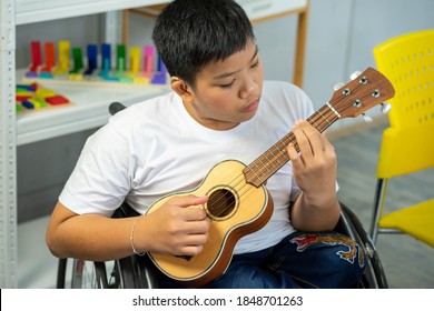 Disability Kid Playing Music With Guitar On Wheelchair With Autism Child Playing In Special Classroom