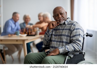 Disabled african american senior man in wheelchair feeling lonely, sitting aside of cheerful elderly men and women playing chess and chatting. Adaptation at retirement house concept - Powered by Shutterstock