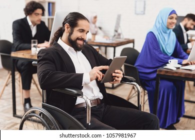 Disabled arab man in suit in wheelchair working in office. Man is talking on tablet.