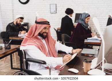 Disabled arab man in thawb in wheelchair working in office. Man is taking notes.