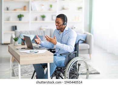Disabled black guy with headset communicating online on laptop, having business meeting from home. Millennial African American man in wheelchair working in call centre remotely