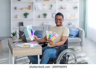 Disabled black guy in wheelchair working as graphic designer online, holding color swatches palette, using laptop at home. Handicapped young man having freelance illustrator or developer job - Powered by Shutterstock