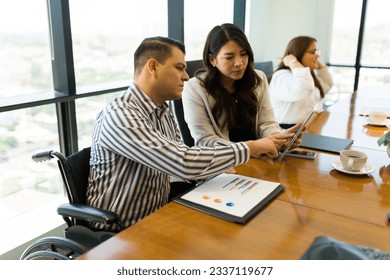 Disabled businessman pointing at digital tablet and discussing with female colleague sitting by in office meeting room - Powered by Shutterstock