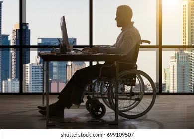 Disabled Businessman Sitting In Wheelchair Using Computer At Workplace