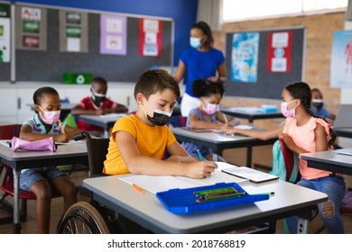 Disabled caucasian boy wearing face mask studying while sitting on wheelchair at elementary school. education back to school health safety during covid19 coronavirus pandemic.