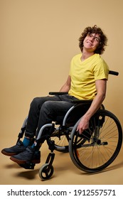 disabled cheerful handicapped man touching wheels and sitting in profile while moving ahead isolated in studio, smile. isolated on beige background