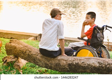 Disabled child on wheelchair and his dad, Sitting by the pond in the city park of Thailand, Sun set in the summer season, Life in the education age of special Children, Happy disabled kid concept.